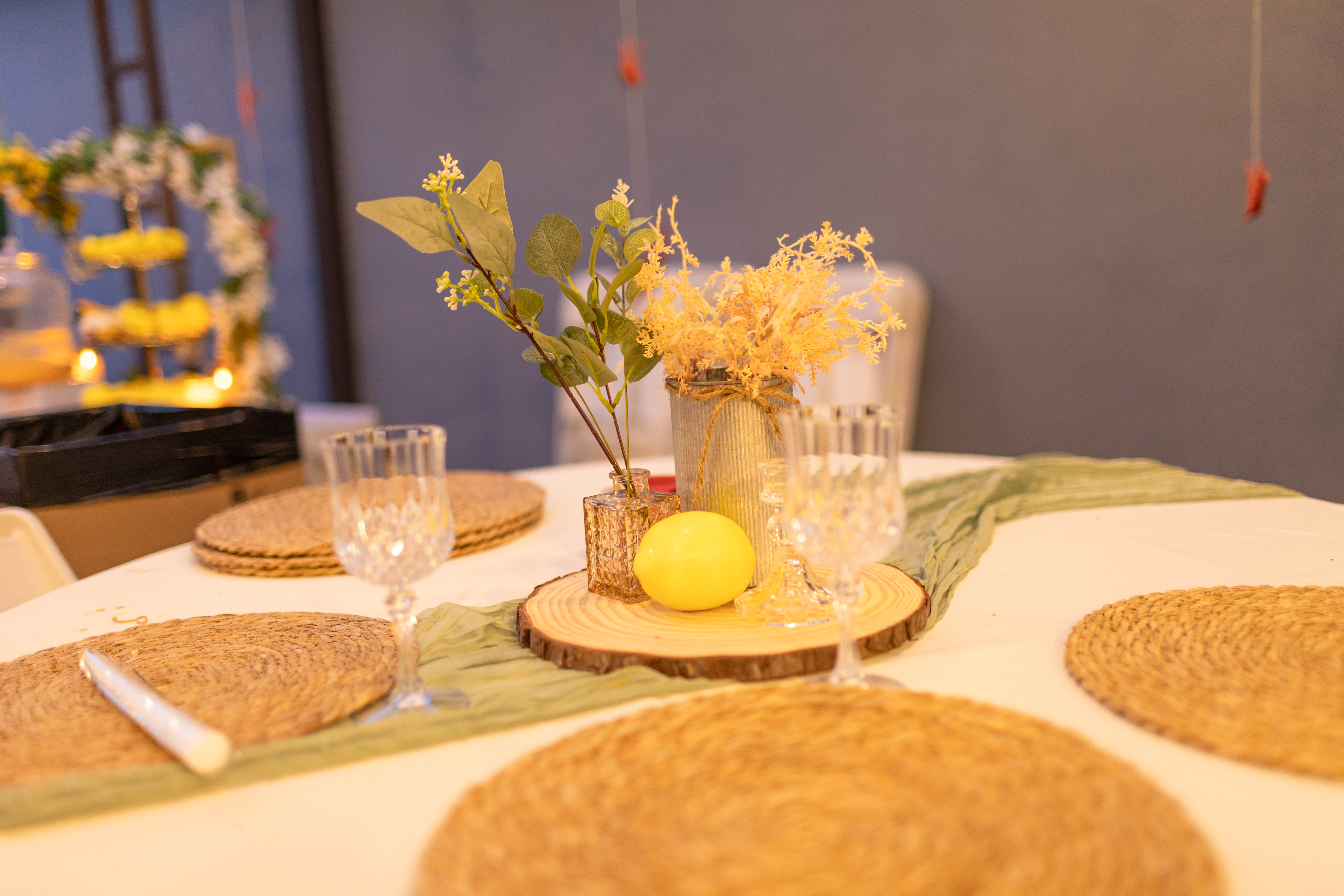 Table centrepiece on a wood slice with botanical stems, amber vases, and crystal glassware on wicker placemats